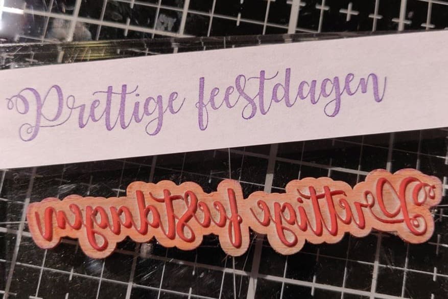 Een lasergesneden stempel met de tekst 'Prettige feestdagen' en de afdruk ervan