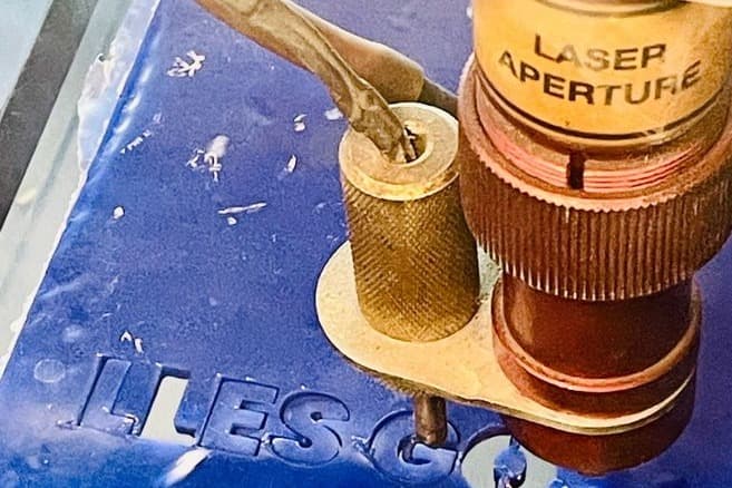 Kop van de lasercutter boven een blauwe acrylplaat met uitgesneden letters